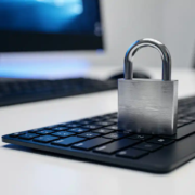 cybersecurity-slot-toetsenbord-kantoor.jpg Gesloten stalen hangslot op een modern toetsenbord in een kantooromgeving, verlicht door blauw monitorlicht.