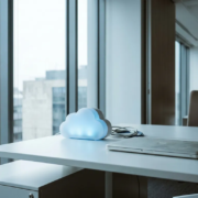 Glanzende cloud-server op wit bureau naast een stoffige laptop in een modern kantoor met groot raam en natuurlijk daglicht.