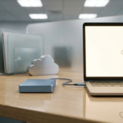 Externe harde schijf en laptop op modern bureau met USB-kabel en gestapelde mappen, symboliserend digitale gegevensopslag.