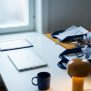 it-kosten-laptop-factuur-bureau.jpg Opgeruimd bureau met laptop en gelamineerde factuur naast een rommelige stapel papieren facturen, USB-sticks en verstrengelde kabels.