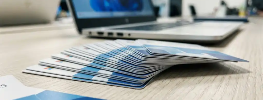 Uitgewaaierde Microsoft 365-licentiekaarten op een modern bureau, met een laptop op de achtergrond in blauw- en zilvertinten.