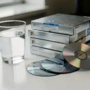 microsoft-software-dozen-glas-bureau.jpg Halfvol glas water naast gestapelde, ongeopende Microsoft-softwaredozen op wit bureau, met cd's die uit een doos vallen.