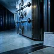 beveiligde-serverruimte-kluis-compliance-infrastructuur.jpg Zware stalen kluisdeur op een kier met verlichte serverruimte op de achtergrond en nalevingschecklist tegen de deurpost.