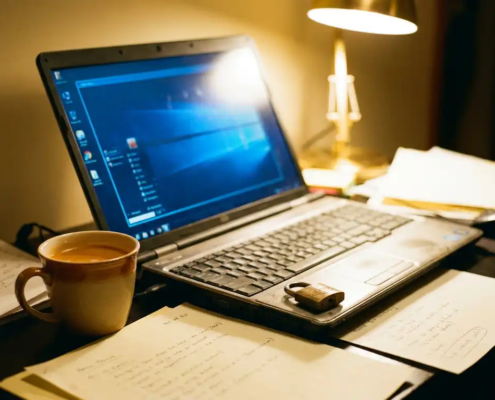 Laptop op thuiskantoor bureau met koffiemok, papieren en klein hangslot naast het toetsenbord, warm licht en blauw schermgloed.