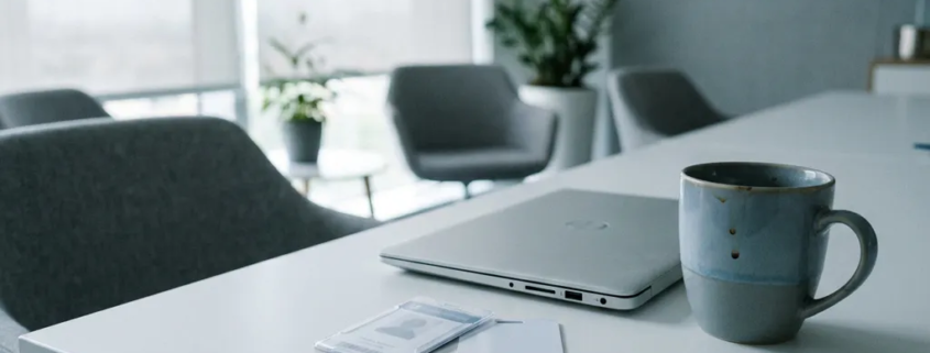 Verlaten toegangspas en keycard op wit bureau naast gesloten laptop en lege koffiemok in modern kantoor.