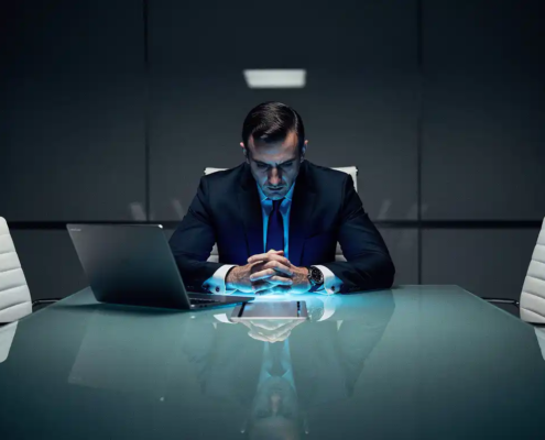 Zakenman in donker pak aan glazen vergadertafel, verlicht door koud blauw laptopscherm in donkere boardroom.