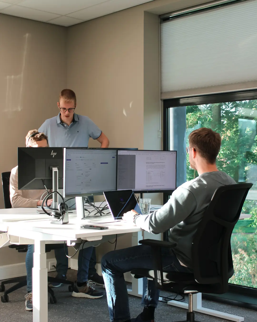 Drie medewerkers van Puur ICT aan het werk, waarvan twee samen naar een computerscherm kijken en één zelfstandig werkt.