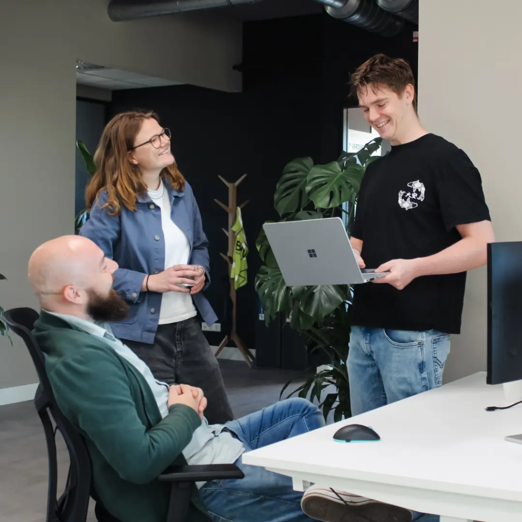 Copilot AI Training Twee collega’s van Puur ICT staan bij het bureau van een andere collega en zijn met elkaar in gesprek.