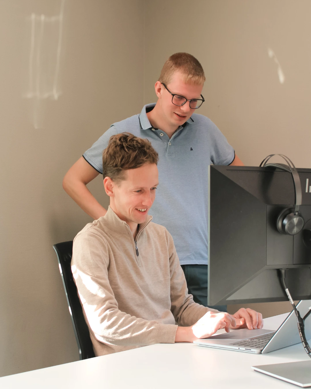 Twee medewerkers van Puur ICT kijken samen naar een computerscherm, één zittend en één staand achter het bureau.