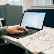 Gefrustreerde kantoormedewerker boven doorgestreept papieren formulier met inktvlekken, laptop op achtergrond als digitaal alternatief.